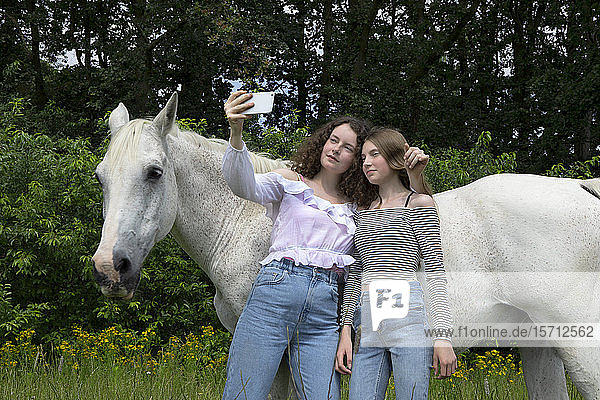 Zwei beste Freunde stehen vor einem Pferd  das sich mit einem Smartphone selbstständig macht