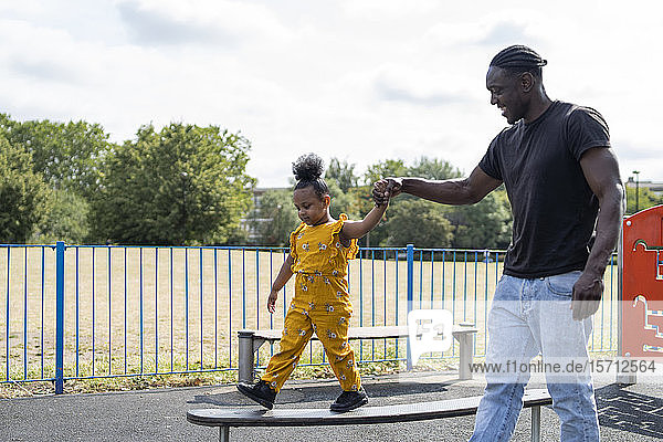 Vater hilft Tochter beim Balancieren auf einer Plattform auf einem Spielplatz