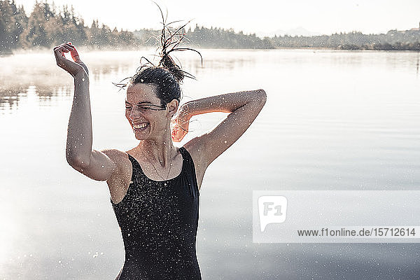 Fröhliche Frau im schwarzen Badeanzug an einem See im Morgennebel