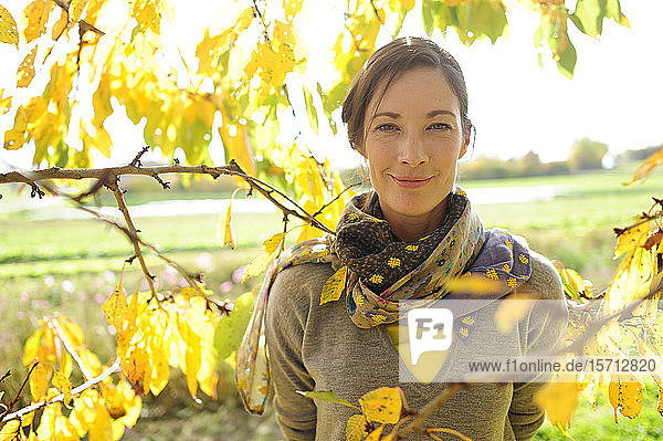 Porträt einer Frau an Zweigen mit Herbstlaub  die in die Kamera schaut