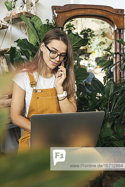 Junge Frau mit Laptop am Telefon in einem kleinen Gartenbaubetrieb