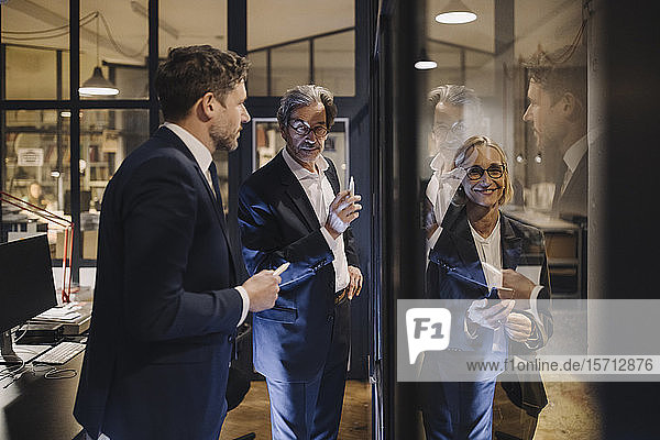 Smiling businesswoman and two businessmen working on drawing on glass pane in office