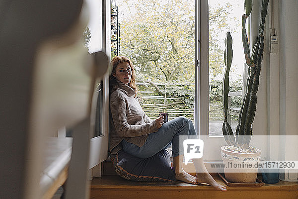 Reife Frau sitzt auf Stufen einer Balkontür und trinkt Kaffee