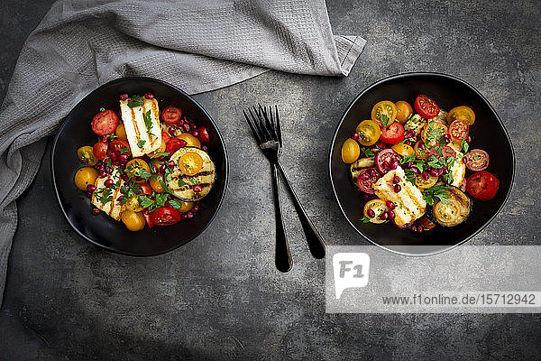 Schalen mit persischem Salat mit Tomaten  gegrilltem Halloumi-Käse  Auberginen  Granatapfelkernen  Sumach  schwarzem Sesam und Petersilie