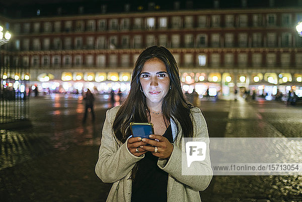 Porträt einer Frau  die nachts auf der Plaza Mayor ihr Smartphone benutzt  Madrid  Spanien