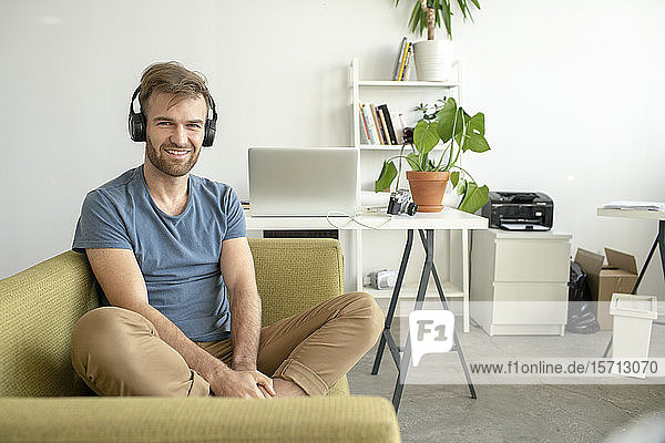 Porträt eines lächelnden Mannes  der im Büro auf der Couch sitzt und Musik hört