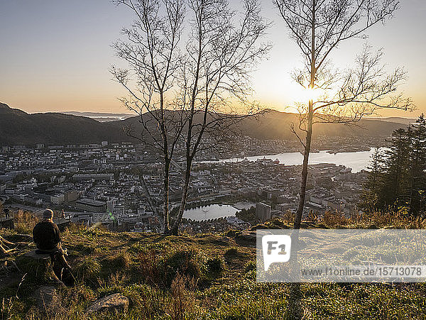 Norwegen  Bergen  Person  die den Sonnenuntergang vom Gipfel eines Hügels mit Blick auf die Küstenstadt bewundert