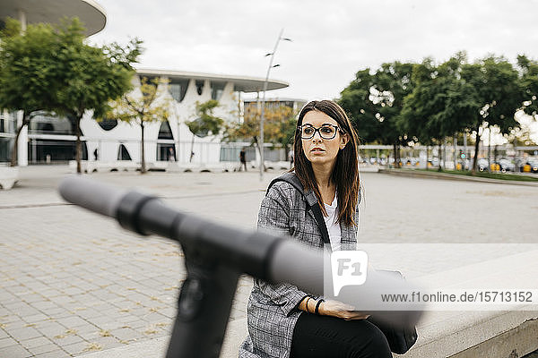 Young businesswoman with e-scooter in the city looking sideways