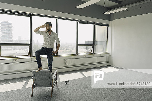 Mature businessman standing on armchair in empty office