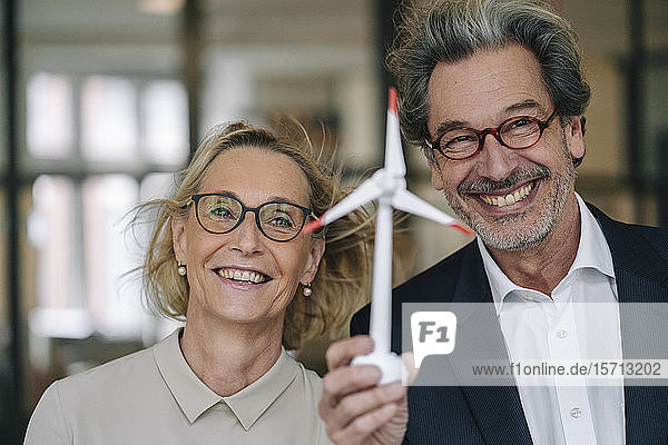 Porträt eines glücklichen Geschäftsmannes und einer glücklichen Geschäftsfrau mit einem Modell einer Windkraftanlage im Amt