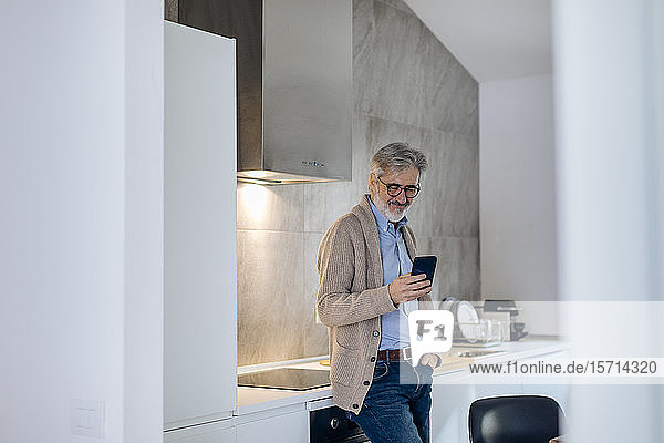 Erwachsener Mann benutzt Mobiltelefon in der Küche zu Hause