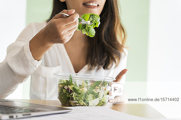 Schrägansicht eines jungen Architekten  der am Schreibtisch gemischten Salat isst
