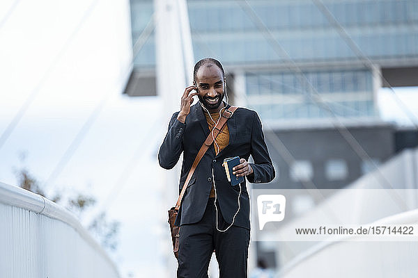 Lächelnder junger Geschäftsmann benutzt Smartphone und Kopfhörer im Freien