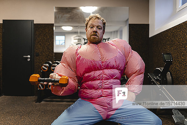 Mann in Turnhalle in rosa Bodybuilder-Kostüm beim Heben einer Hantel