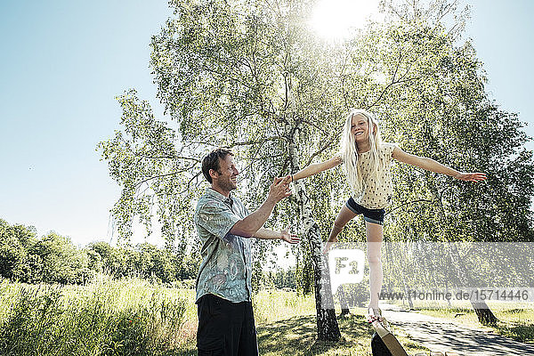 Vater hilft Tochter beim Balancieren auf einer Parkbank