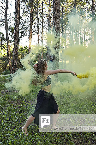 Junge Frau tanzt mit gelb gefärbtem Rauch im Wald