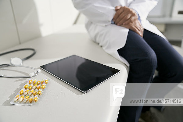 Arzt  der in seiner Praxis mit Tablette  Stethoskop und Kapseln auf dem Tisch sitzt