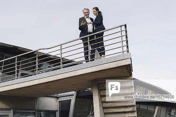 Geschäftsmann und Geschäftsfrau benutzen Tablette auf einem Balkon vor dem Bürogebäude
