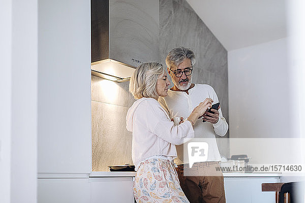 Ein erwachsenes Paar benutzt zu Hause in der Küche ein Mobiltelefon