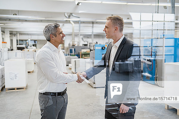 Two businessmen shaking hands in a factory