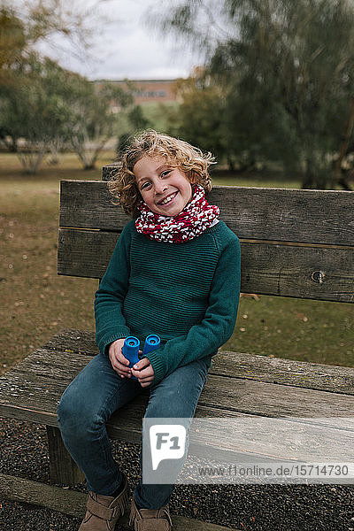 Porträt eines glücklichen Jungen mit Fernglas  der im Herbst auf einer Bank sitzt