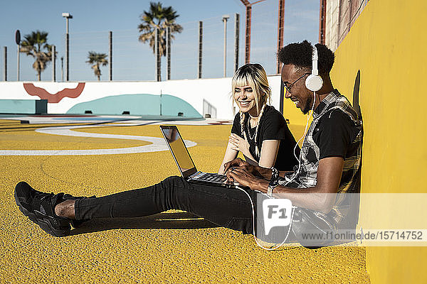 Lächelndes junges Paar benutzt Kopfhörer und Laptop im Freien