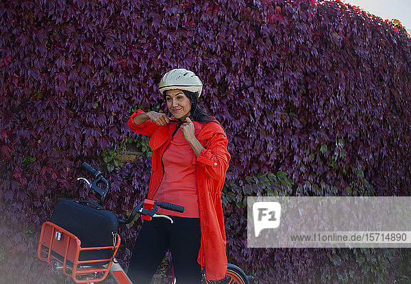Junge Frau sitzt auf Fahrrad  setzt Schutzhelm auf