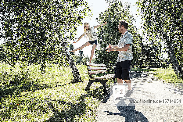 Vater beobachtet Tochter beim Balancieren auf einer Parkbank