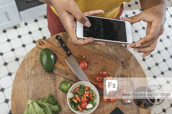 Nahaufnahme einer Frau in der Küche  die eine gesunde Mahlzeit zubereitet und ein Smartphone in der Hand hält