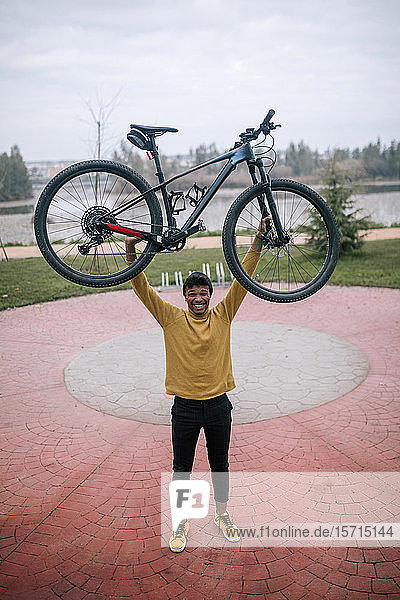 Porträt eines glücklichen jungen Mannes  der ein Fahrrad hebt