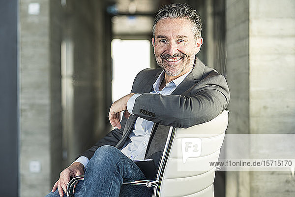 Porträt eines lächelnden reifen Geschäftsmannes  der auf einem Stuhl im Büro sitzt