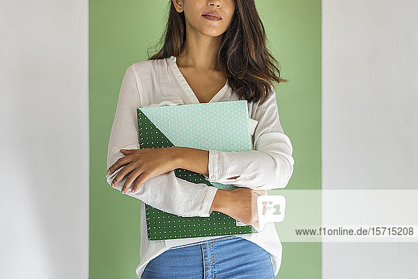 Crop view of young businesswoman standing in front of green wall holding folder