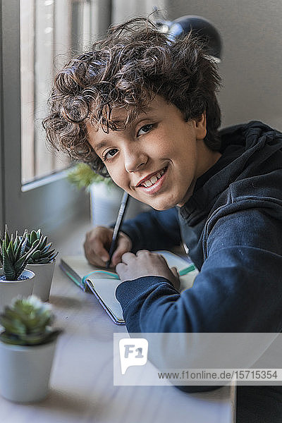Porträt eines lächelnden Jungen  der am Fenster Notizen macht