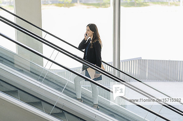 Smiling businesswoman on escalator talking on the phone