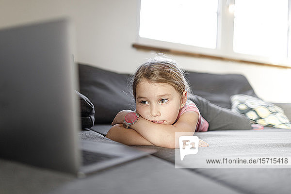 Girl lying on couch at home looking at laptop