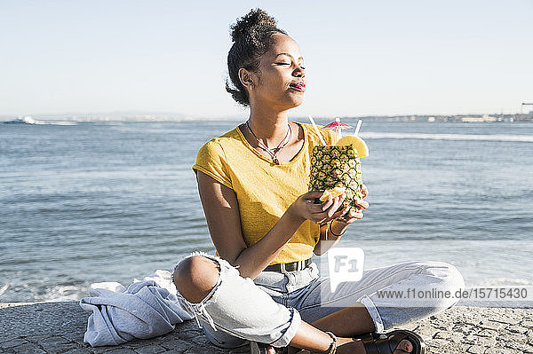 Junge Frau sitzt am Wasser und genießt ein Getränk in einer Ananas  Lissabon  Portugal