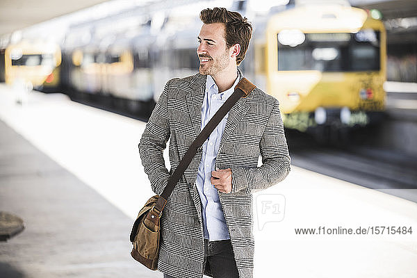 Smiling young businessman at the train station looking around
