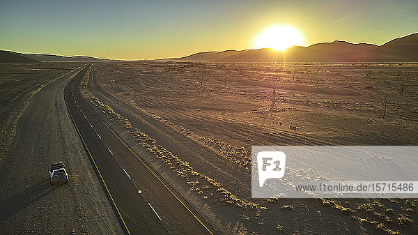 Jeep auf schmutziger Piste in der Namib-Wüste mit der Sonne hinter den Dünen versteckt  Namibia