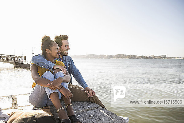 Junges Paar sitzt am Pier am Wasser und genießt die Aussicht  Lissabon  Portugal