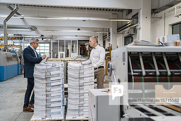 Two businessmen at stack of papers in a factory