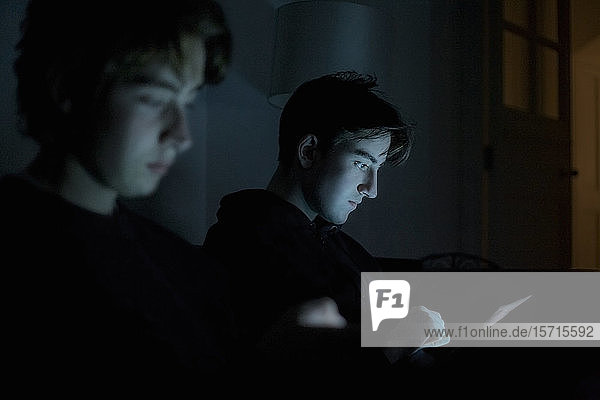 Zwei Teenager  die zu Hause im Dunkeln mit Technik umgehen