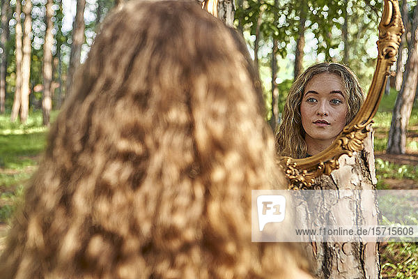 Rückenansicht einer jungen Frau  die ihr Spiegelbild in einem Wald betrachtet