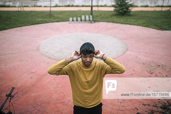 Porträt eines selbstbewussten jungen Mannes im Freien  der sich eine Mütze anzieht