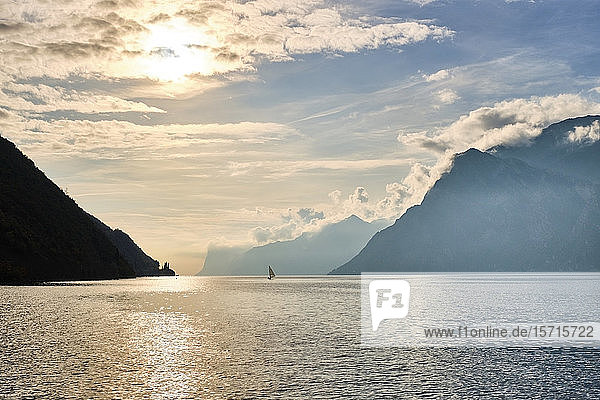 Italy  Trentino  Nago-Torbole  Silhouette of sailboat sailing near coastal cliffs of Lake Garda at moody sunrise