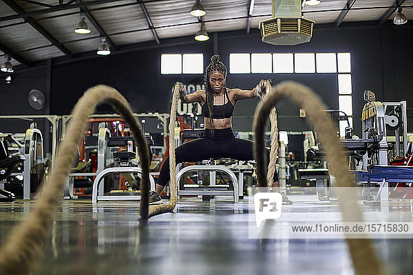 Female athlete doing strength training with heavy ropes in gym