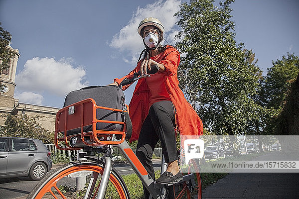 Junge Frau mit Helm und Gesichtsmaske  Fahrradfahren in der Stadt