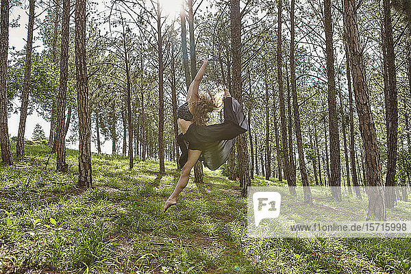Barfüßige junge Frau springt im Wald in die Luft