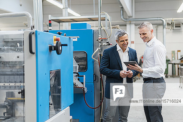 Two smiling businessmen with tablet talking in a factory
