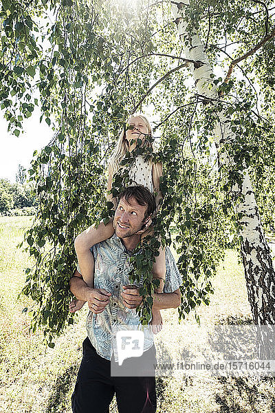 Vater trägt Tochter huckepack unter einer Birke