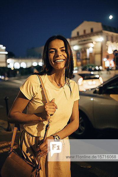 Junge lächelnde Frau in der Stadt bei Nacht